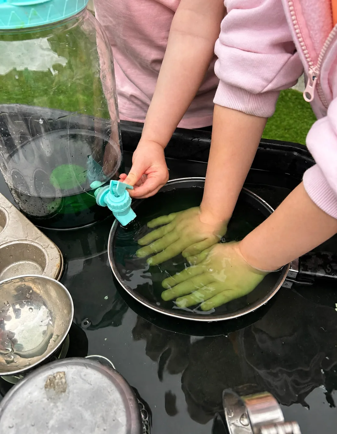 A child using their hands and a small tool to explore ice and water in bowls