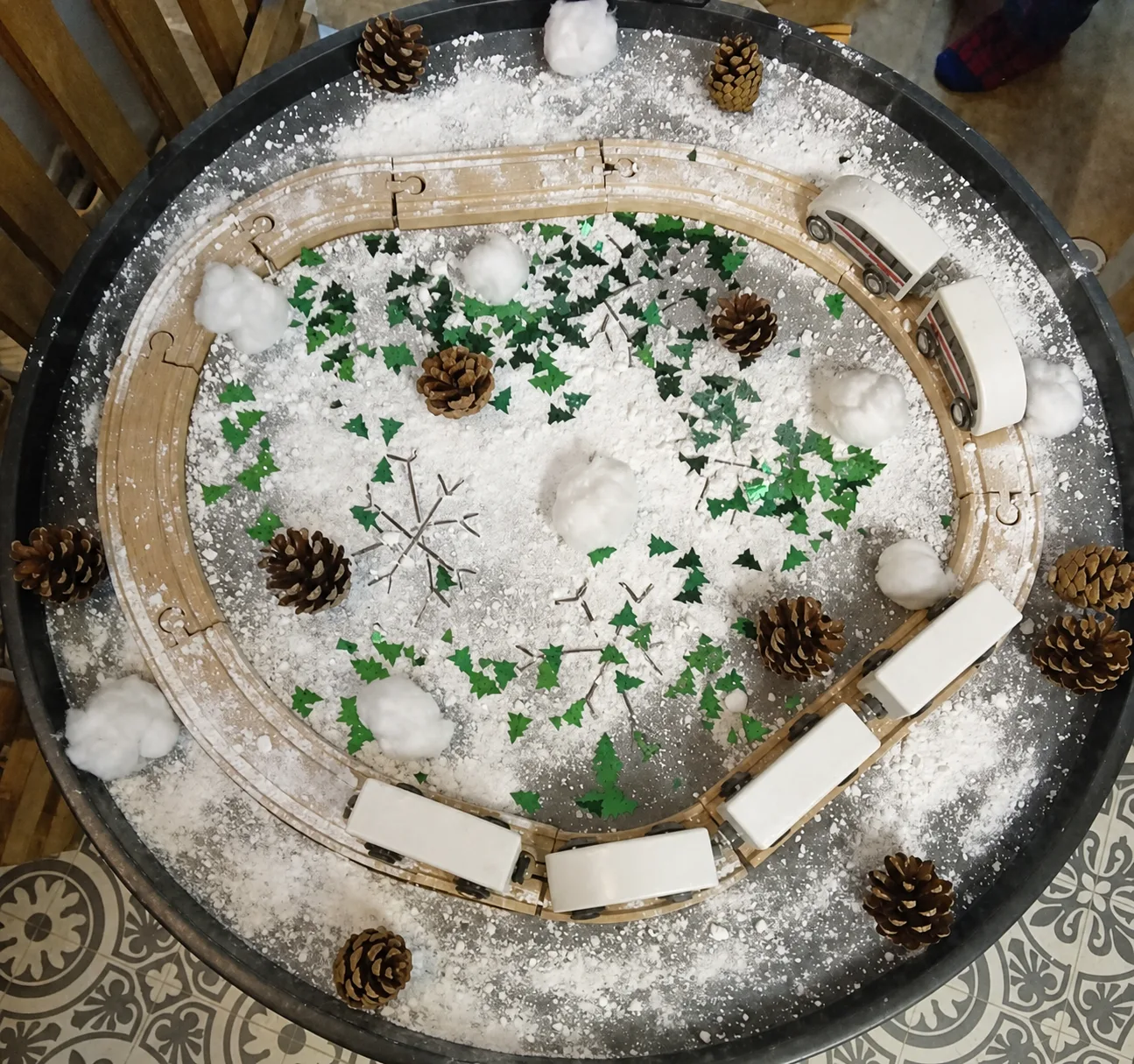 A winter-themed sensory tray with artificial snow, pinecones and natural materials