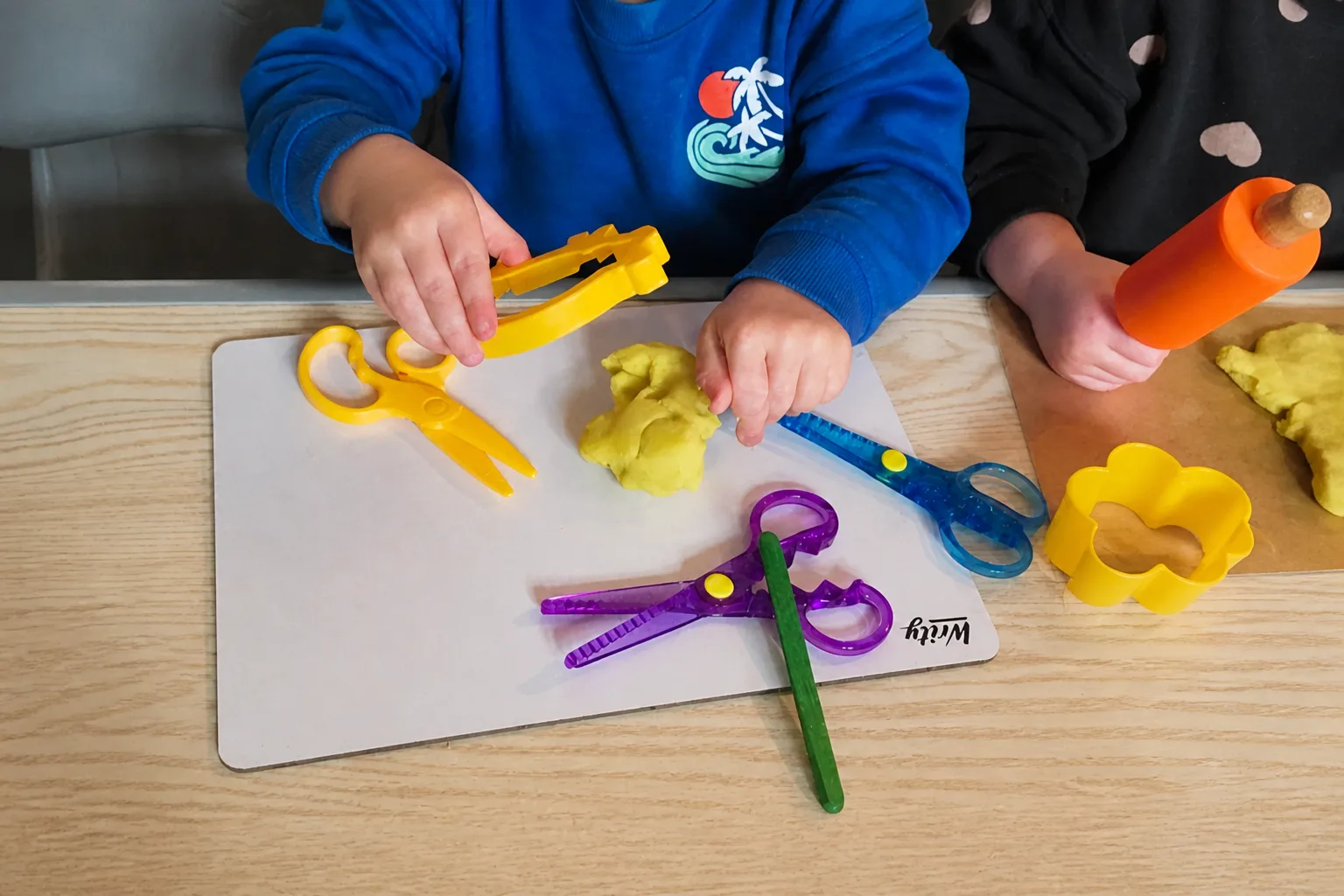 Children using colourful tools to roll, cut and shape playdough at a table