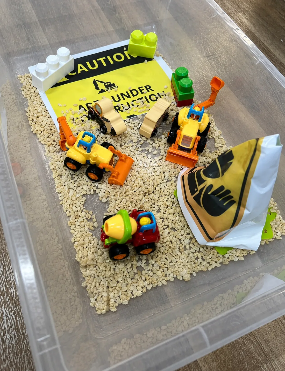 Toy construction vehicles and themed props arranged in a textured sensory tray