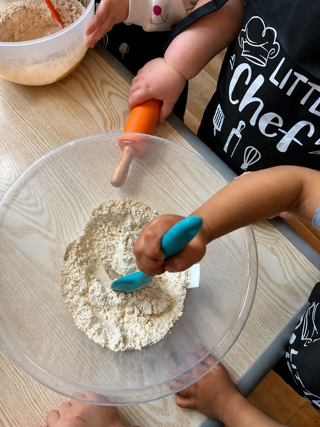 Children using colourful utensils to mix flour in a large bowl